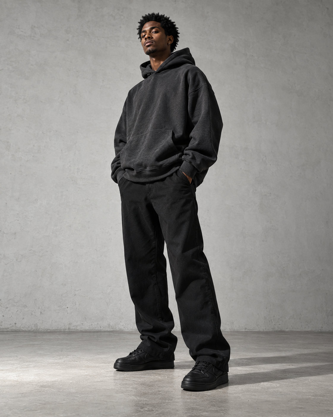 Model wearing an oversized charcoal hoodie in a concrete studio